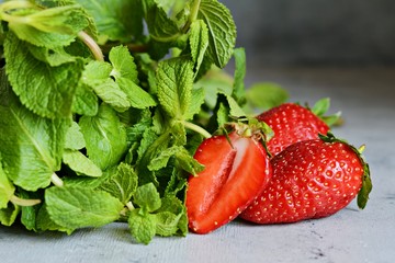 Ripe juicy strawberries with a bunch of fragrant fresh mint on a blue background. Greens and fruits for the summer drink.
