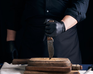 chef in a black shirt and black latex gloves holds a vintage kitchen knife
