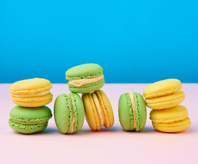 stack of yellow and green round almond flour cakes macarons with cream on a blue background