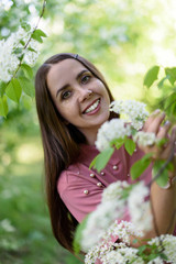 Fototapeta premium Portrait of happy girl in a pink t shirt holding flowering cherry branch and looking at the camera in sunny spring day in park