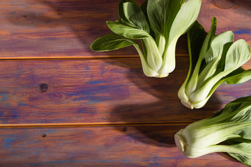 Fresh green bok choy or pac choi chinese cabbage on a colored wooden background. Side view, selective focus, copy space.