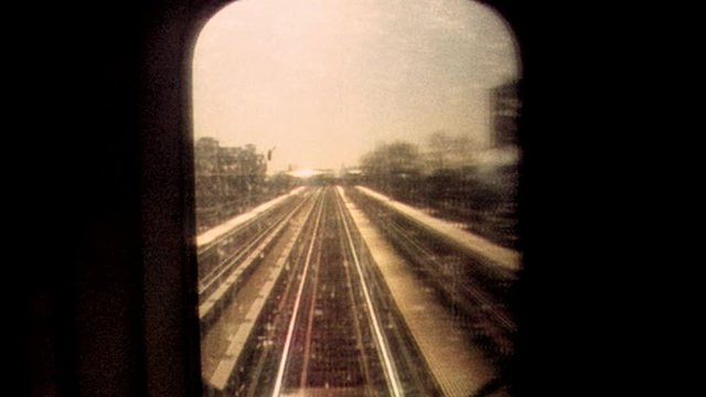 Retro looking archival footage filmed on New York City subway looking out through subway window at tracks and passing train as sun sets in the distance