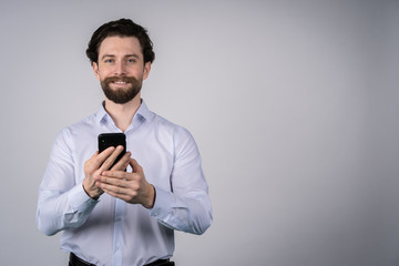 Young man with beard in white shirt, looks straight into the camera and keeps the phone, the concept of a business man