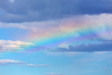 Rainbow in the blue sky with clouds over sea