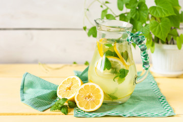 Lemonade with lemon and mint in a jug on a yellow rustic table.