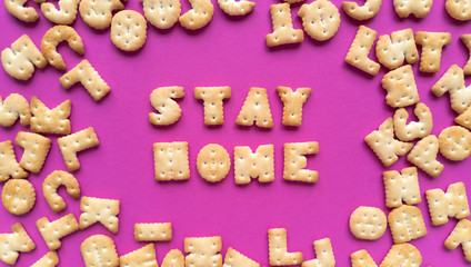Stay home. Quarantine quote from crackers on pink background and scattered letters. Simple flat lay with pastel texture. Stock photo.