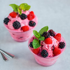 Homemade berry sorbet in glass cups, mint leaves and fresh berries on gray background.
