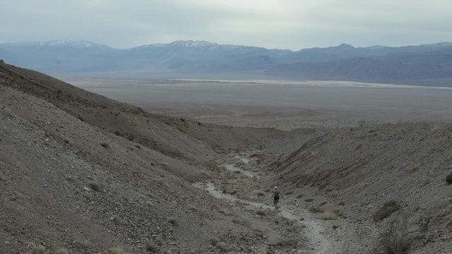A male hiker exits Fall Canyon via a wash. Death Valley National Park in California. The Panamint Mountain Range is seen in the distance.