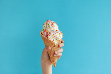 Children's hand holds delicious vanilla ice cream cone on a blue background.