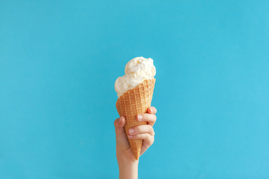 Children's hand holds delicious vanilla ice cream cone on a blue background.