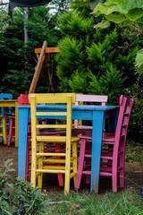 Fototapeta na wymiar multi-colored wooden table and chairs in the summer garden at the cottage