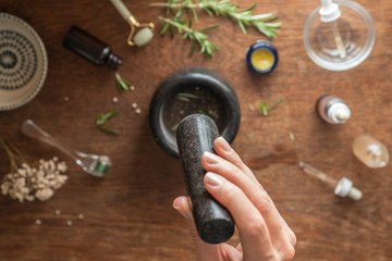 Close up of woman using pestle and mortar.  Table out of focus with range of ingredients relating to beauty and skin care.  Top down view of beauty background.