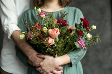 Man and woman holding flowers. Beautiful tulips in man's hands on a background of gray wall. Flowers art design. Man in white shirt with flower present for woman in dress standing in front of him. 