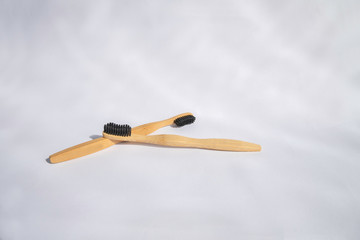 Two light eco bamboo wooden toothbrushes with black bristles lie on a light background in unusual light with highlights