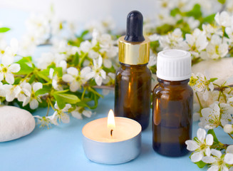 Aromatherapy concept with essential oil bottles, blossom, burning candle and pebbles. Spa or herbal medicine still life composition. Copyspace.