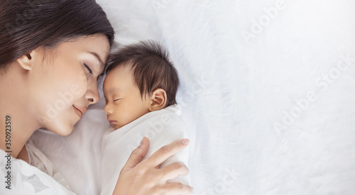 Close up portrait of beautiful young asian or caucasian mother girl kissing her healthy newborn baby sleep in bed with copy space. Healthcare and medical love asia woman lifestyle mother's day concept