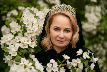 A young beautiful woman stands in the white flowers of an Apple tree and looks directly at the...