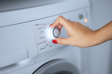 The girl sets the washing program for the washing machine.