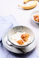 Creamy Rice Porridge or Pudding with caramelized bananas in bowl on grey concrete background. Selective focus
