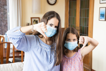 Sisters at home with protective face mask and thumb down