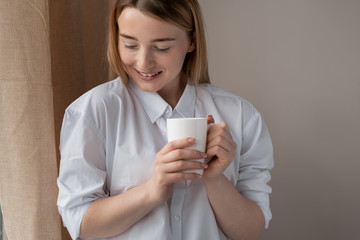 Close up portrait of a blonde woman. He is standing by the window drinking tea.