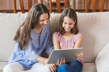 Two smiling girls looking at the tablet at home