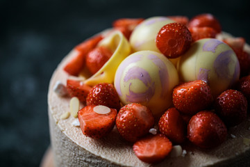 Cake with strawberry and chocolate spheres is located on dark background. Closeup decor.