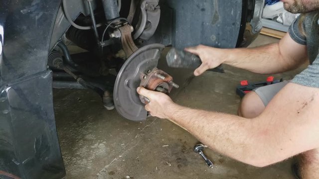 Man removes bearings from his passenger car front wheel preparing for new replacement.
