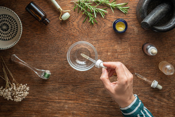 Woman's hand shown using a pipette to dispense facial oil into glass bowl.  Beauty skin care theme background with natural rustic atmosphere.