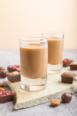 Sweet chocolate liqueur in glass on a gray concrete background and stone slate board. Side view, selective focus.
