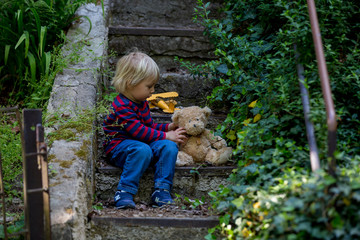 Cute little todller boy, sitting on stairs with teddy bear