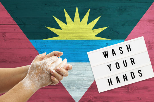Antigua and Barbuda flag background on wooden surface. Minimal wash your hands board with minimal international hygiene concept hand detail.
