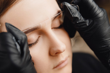 Master applies thread to woman on brow. Correction and tinting eyebrows