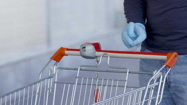 Buyer cleans handle of shopping cart with a disinfectant and an antibacterial wipe before shopping at store. Sanitary measures in public place during quarantine. Virus protection.