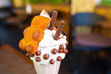 Cool milkshake with cookies and chocolate balls. Milkshake in a glass beaker on a table on a street platform in a cafe. Refreshing summer drinks