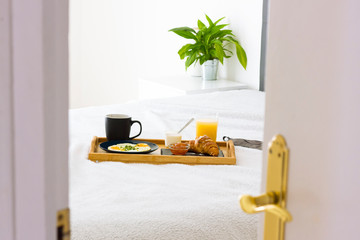 opened white door to bedroom interior with bed, plant and decorative set of breakfast on the bed....