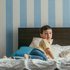 cute kid looking at camera while crawling on bed at home