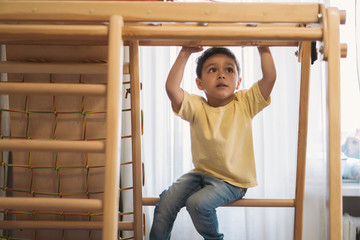 adorablle boy exercising in home gym while sitting on ladder