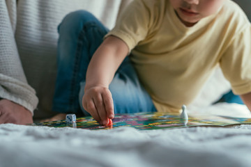 cropped view of little boy playing board game on bed, selective focus
