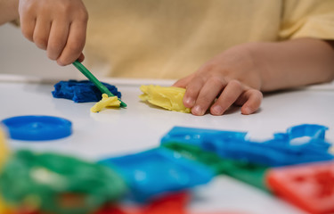 Naklejka premium cropped view of little boy cutting colorful plasticine with spatula
