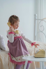 little girl talks by retro phone sitting on the bed with ruffled pillows