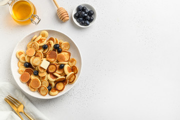 Tiny trendy pancakes with blueberry and honey on white background. View from above. Copy space.