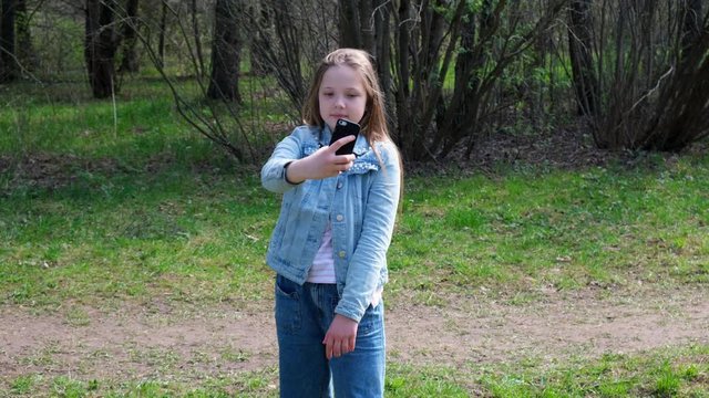 Young teenager girl making selfie photo with smartphone. Girl walking in the park in sunny day. 4k footage.