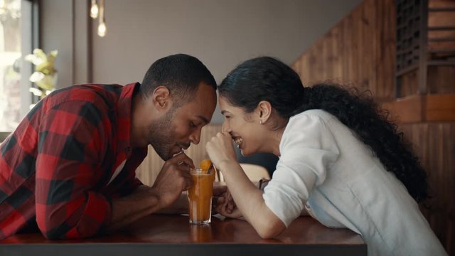 Loving young couple drinking juice from one glass at a cafe and smiling. African man and woman enjoying together on a date.
