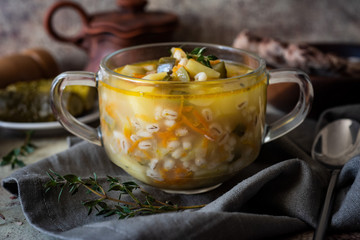 Rich soup with meat, pickles and vegetables in a glass plate on a gray background close-up.