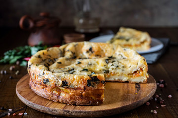 Fototapeta premium Delicious pie with cabbage and herbs on a wooden platter close-up on a wooden table, in the background a piece of pie on a plate