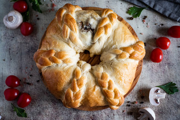 Ruddy yeast pie with mushrooms on a wooden platter on a gray background. The view from the top