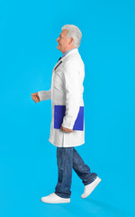 Senior doctor with clipboard walking on light blue background