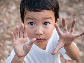 Asian cute little child boy showing dirty black hands while playing outdoor. Happy kid enjoy in relaxing day, preschool learning and freedom concept.