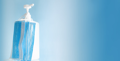 Bottle Dispenser alcohol gel to sanitize hands medical face masks, surgical protective disposable face mask on blue background. Coronavirus covid virus prevention, hand hygiene web banner copy space